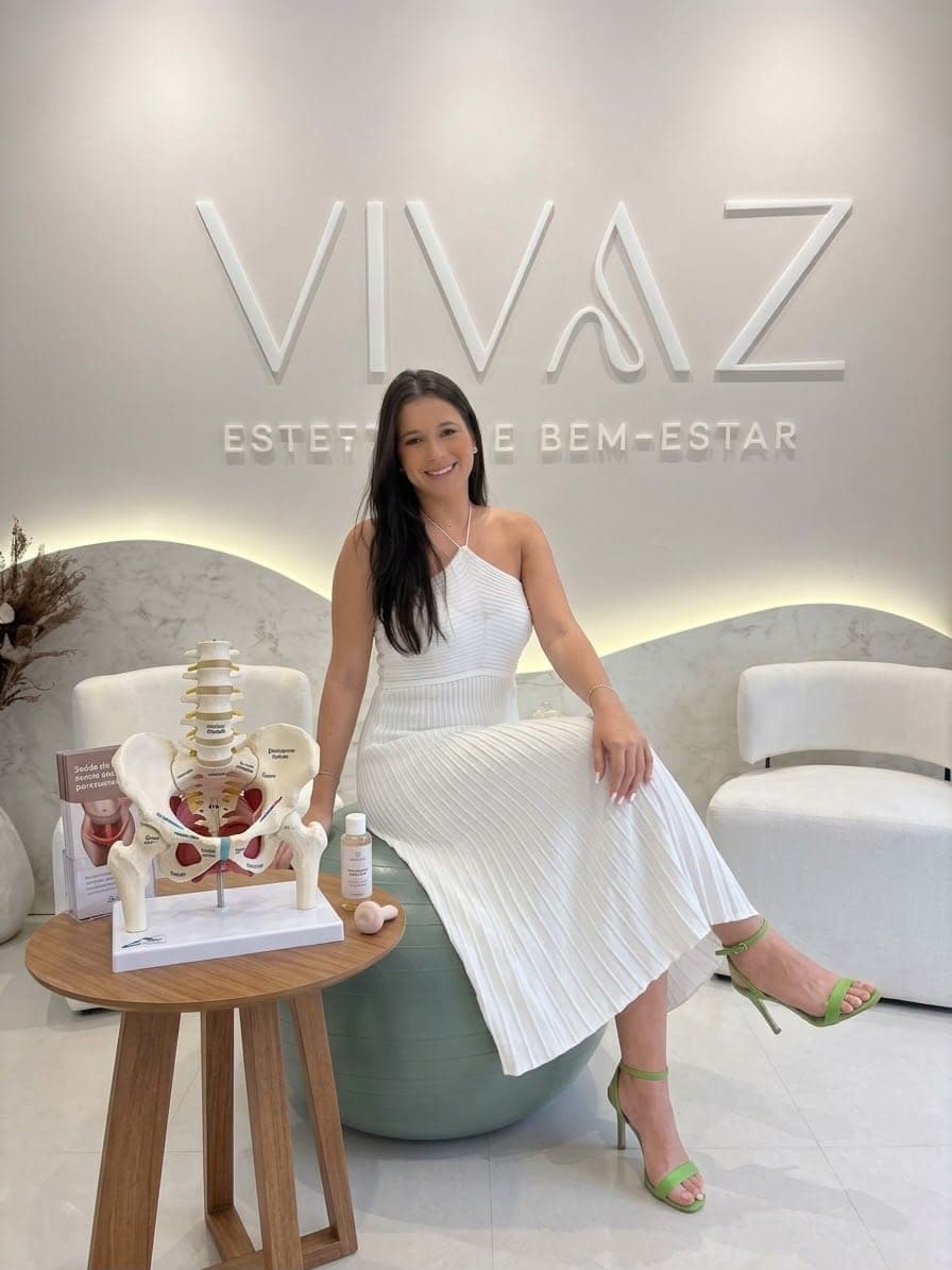 Dra. Carolina Vaz sentada numa bola de pilates, ao lado de um modelo anatômico de pelve