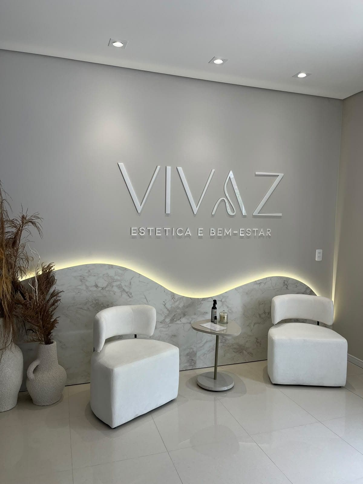 Recepção da Vivaz, com o logo na parede, faixa de mármore iluminada e duas poltronas brancas